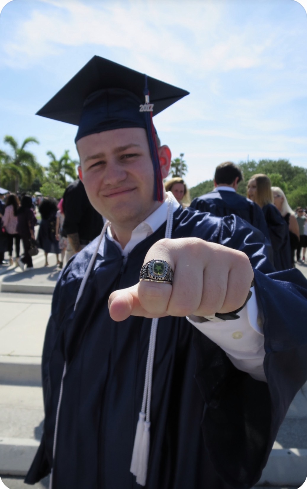 Stephen in his cap and gown showing his class ring on graduation day
