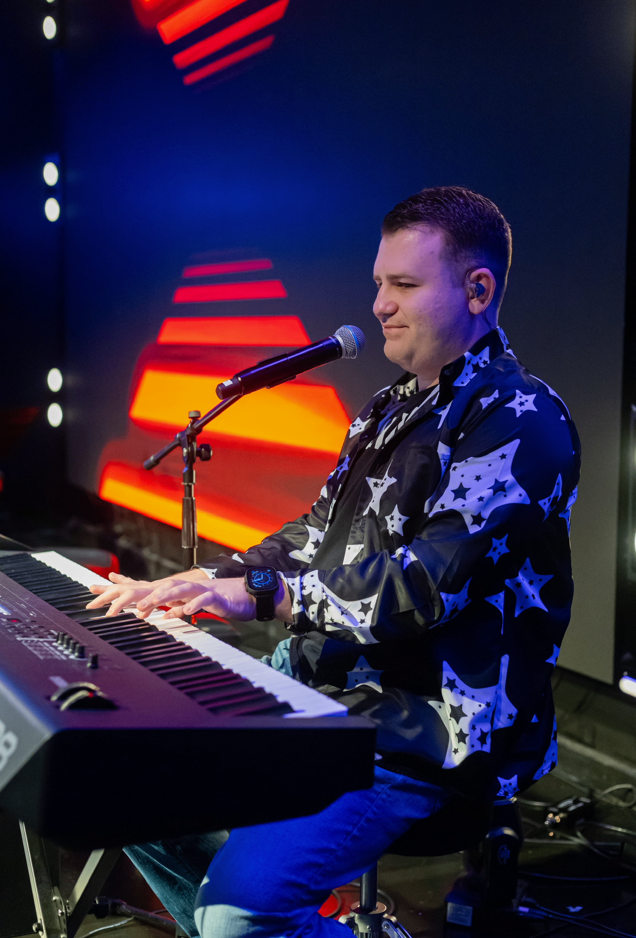 Stephen Lepore performing at the piano and singing into a microphone under stage lights