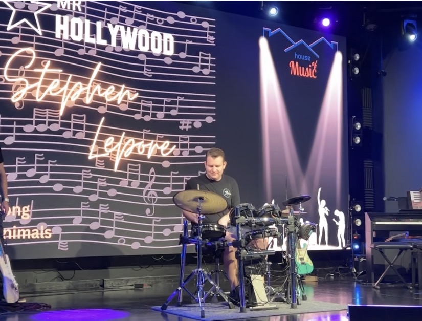 Stephen Lepore playing the drums on stage in front of a Mr. Hollywood Stephen Lepore screen