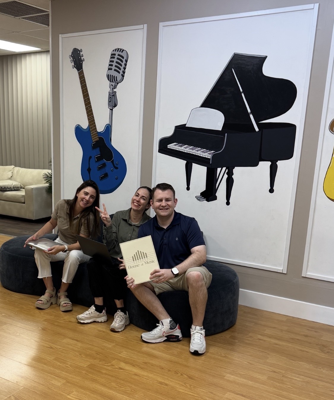 Stephen Lepore sitting with his House of Music coworkers in front of the instrument murals