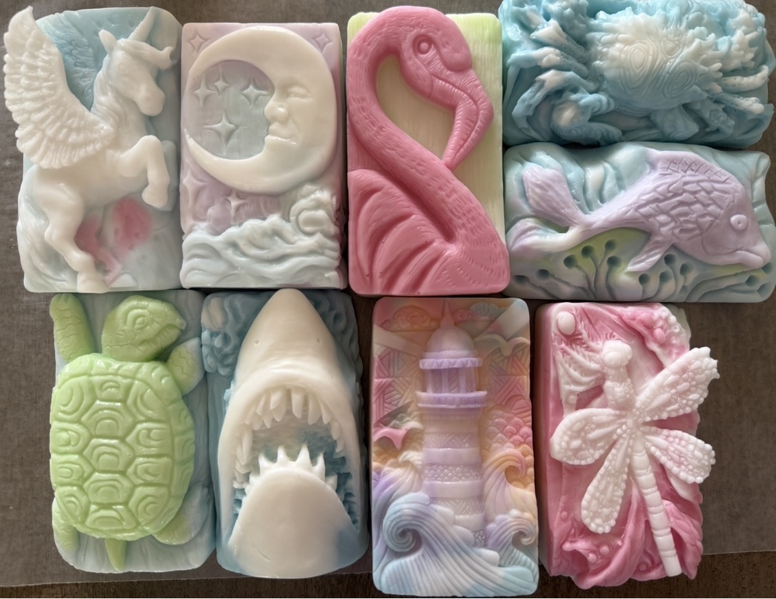 Close up arrangement of finished decorative soaps shaped like a unicorn, moon, flamingo, turtle, shark, lighthouse and dragonfly